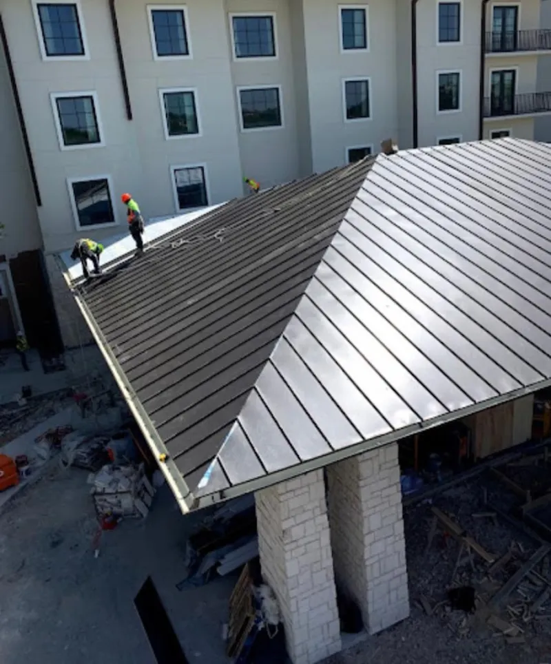 Crew installing standing seam metal roof panels on a commercial project in Oshtemo